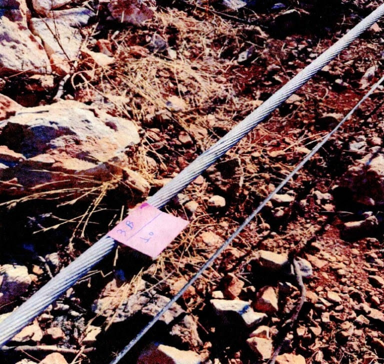 Στην πρώτη φωτογραφία διακρίνεται τμήμα αγωγού ηλεκτρικής ενέργειας που φέρει εμφανή ίχνη ανάπτυξης ηλεκτρικού τόξου. Συγκεκριμένα, καταγράφονται τοπική τήξη και παραμόρφωση των εξωτερικών αλουμινένιων κλώνων, ευρήματα που, σύμφωνα με το πόρισμα της Πυροσβεστικής Υπηρεσίας, είναι συμβατά με την εκδήλωση βραχυκυκλώματος.


